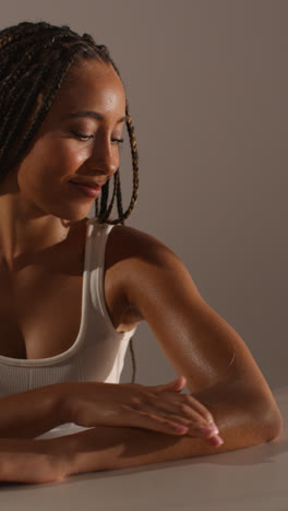 Studio-Skincare-Beauty-Shot-Of-Young-Woman-With-Long-Braided-Hair-Putting-Moisturiser-Onto-Arm-And-Shoulder